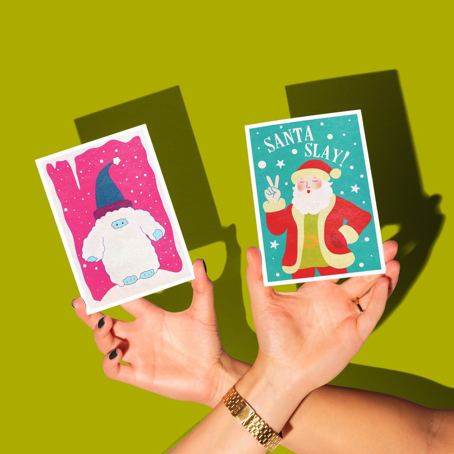 Two hands holding Christmas-themed cards against a green background
